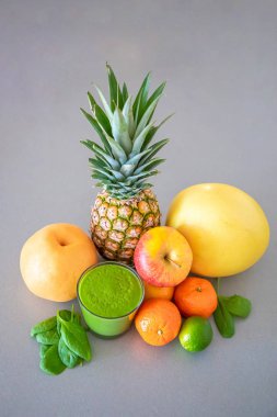 Gri arka planda farklı tropikal meyveler ve yeşil smoothie, sağlıklı beslenme tarzı konsepti