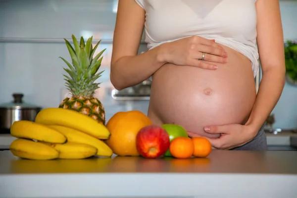 Mujer embarazada y diferentes frutas tropicales en la cocina casera — Foto de Stock