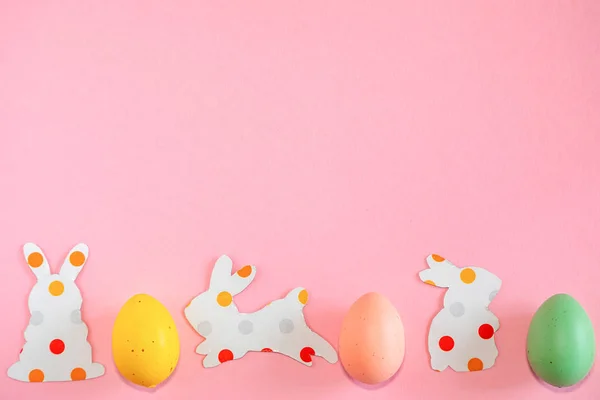Oeufs de Pâques colorés et silhouettes en papier d'un lapin de Pâques sur fond rose — Photo