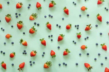 Pastel yeşil arka planda çilek ve yaban mersini. Düz yatıyordu, yiyeceklerin en üst görüntüsü.
