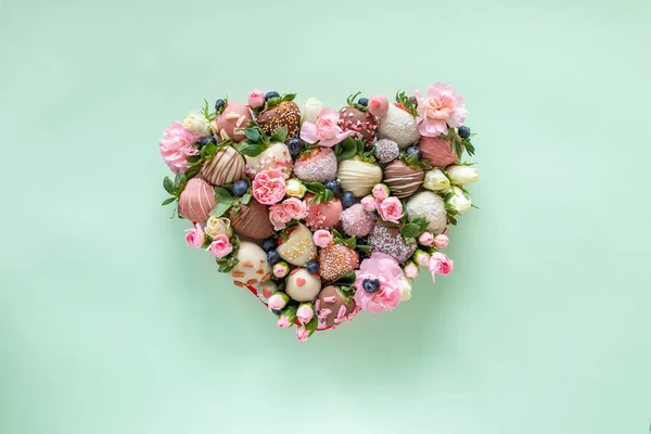 Hartvormige doos met handgemaakte chocolade bedekt aardbeien met verschillende toppings en bloemen als geschenk op Valentijnsdag op groene achtergrond — Stockfoto