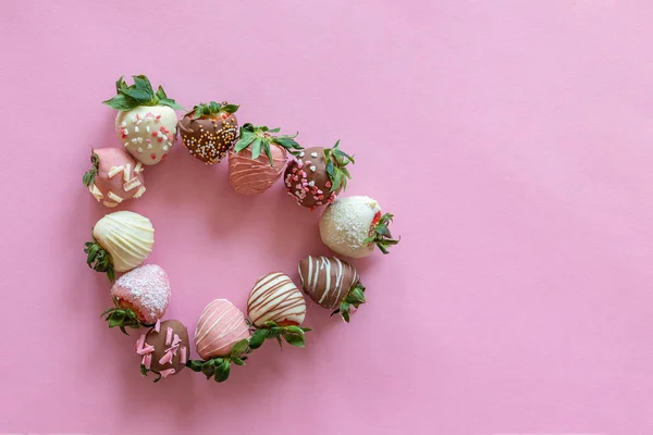 Coeur en forme de fraises recouvertes de chocolat à la main avec différentes garnitures sur fond rose — Photo