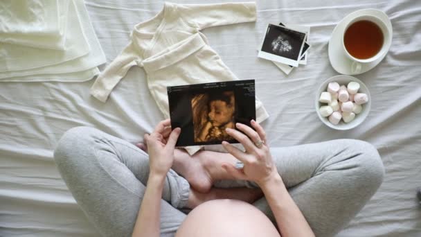 超音波スキャンを見ながら彼女の腹に触れる妊娠中の女性を期待のトップビュー自宅で 妊娠と出産の概念 — ストック動画