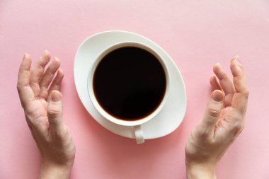 Kadın eli ve pembe arka planda bir fincan kahve, düz yatış, üst manzara.