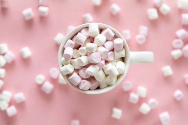 Fincanda pembe ve beyaz şekerlemeler ve pembe arka planda sıcak çikolata.