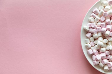 Pembe arka planda beyaz bir tabakta pembe ve beyaz mini şekerlemeler ve metin için boş alan.