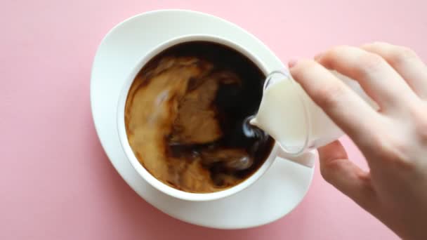 Hand pouring milk into coffee, process mixing coffee and milk in cup on pink background — Wideo stockowe