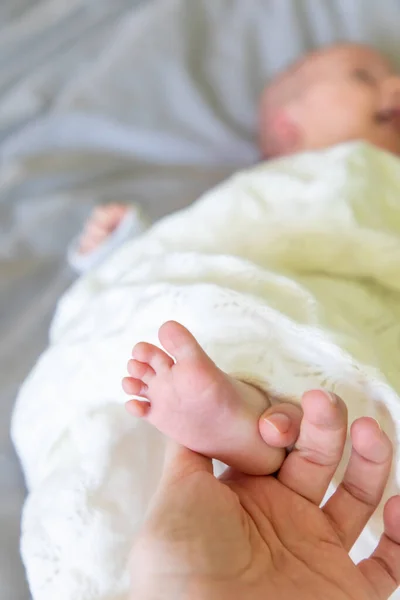 Primer plano pie recién nacido del bebé acostado en la cama en la mano madre — Foto de Stock