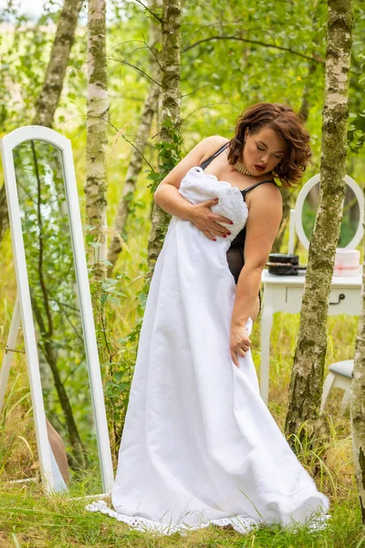 A beauty woman trying on a wedding dress in front of a mirror in the forest, morning of the bride, natural beauty