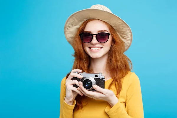 Concetto di viaggio - Primo piano Ritratto giovane bella ragazza dai capelli rossi attraente con cappello alla moda, occhiali da sole e fotocamera vintage sorridente alla fotocamera. Sfondo blu pastello. Copia spazio . — Foto Stock