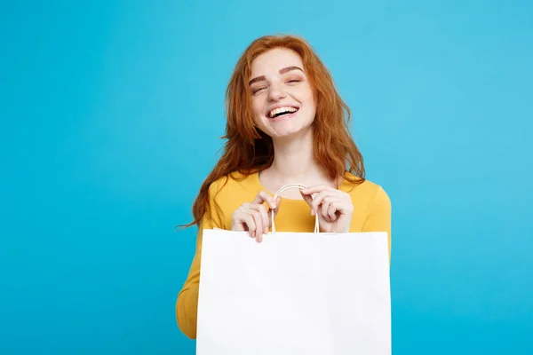 Nákupní koncept - zblízka portrét mladé krásné redhair atraktivní dívka, usmívající se, při pohledu na fotoaparát s bílým nákupní taška. Pastelové modré pozadí. Kopírovat prostor. — Stock fotografie