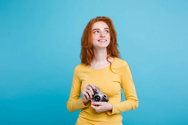 Concetto di viaggio - Primo piano Ritratto giovane bella ragazza dai capelli rossi attraente con cappello alla moda, occhiali da sole e fotocamera vintage sorridente alla fotocamera. Sfondo blu pastello. Copia spazio . — Foto Stock