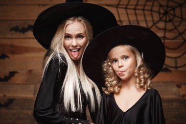 Cadılar Bayramı kavramı - neşeli anne ve kızı cadı kostümleri Cadılar Bayramı ile eğri kabaklar yarasalar ve örümcek ağı ahşap studio arka plan üzerinde poz kutluyor.