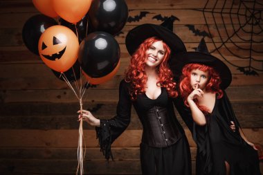 Halloween cadı kavramı - neşeli anne ve kızı cadı kostümleri Cadılar Bayramı yarasalar ve örümcek ağı ahşap studio arka planda turuncu ve siyah balon ile poz kutluyor.