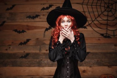 Halloween cadı kavramı - mutlu Cadılar Bayramı Kızıl saçlı cadı holding ile poz yüz eski ahşap studio arka plan üzerinde şok.