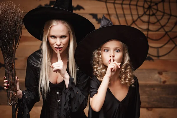 Cadılar Bayramı kavramı - neşeli anne ve kızı cadı kostümleri Cadılar Bayramı ile eğri kabaklar yarasalar ve örümcek ağı ahşap studio arka plan üzerinde poz kutluyor.