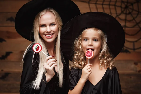 Halloween Concept - allegra madre e sua figlia in costumi da strega che celebrano Halloween in posa con zucche curve su pipistrelli e ragnatela su sfondo studio di legno . — Foto Stock