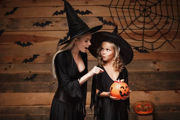 Halloween Concept - mooie Kaukasische moeder en haar dochter in heks kostuums Halloween vieren met delen van Halloween snoep en zoet over vleermuizen en spinnenweb op houten studio achtergrond. — Stockfoto