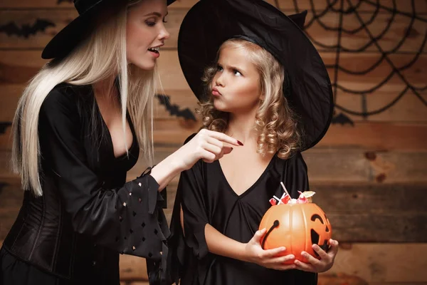 Halloween concept - schöne kaukasische Mutter spielt mit ihrer kleinen Tochter und genießt mit halloween candy und sweet over Fledermäuse und Spinnennetz auf hölzernem Studiohintergrund. — Stockfoto