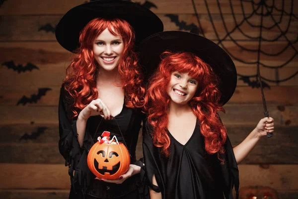 Halloween Concept - mooie Kaukasische moeder en haar dochter met lange rode haren in heks kostuums met Halloween snoep en magic wand. — Stockfoto