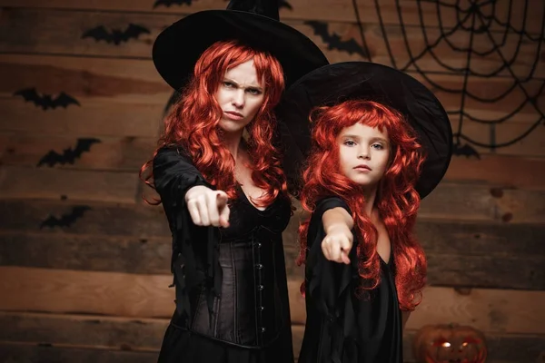 Halloween Concept - mooie Kaukasische moeder en haar dochter met lange rode haren in heks kostuums met boze kieskeurig gelaatsuitdrukking en wijzende vinger naar camera. — Stockfoto