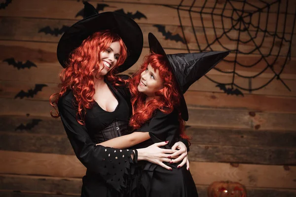 Halloween Concept - mooie Kaukasische moeder en haar dochter met lange rode haren in heks kostuums gelukkig lachend en omhelzen elkaar. — Stockfoto