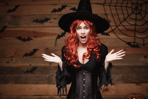 Conceito de bruxa de Halloween - Feliz Halloween cabelo vermelho Bruxa segurando posando com o rosto chocado sobre o velho estúdio de madeira fundo . — Fotografia de Stock