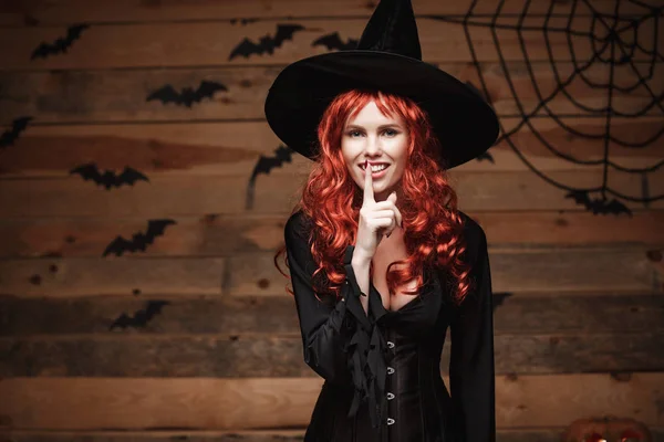 Concept de sorcière Halloween - Joyeux Halloween cheveux roux Sorcière faire geste de silence avec le doigt sur les lèvres sur un vieux fond de studio en bois . — Photo