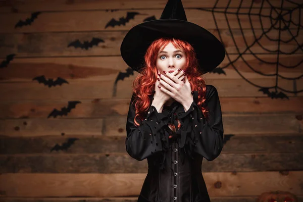 Halloween heks concept - Happy Halloween rood haar heks bedrijf poseren met gezicht geschokt over oude houten studio achtergrond. — Stockfoto