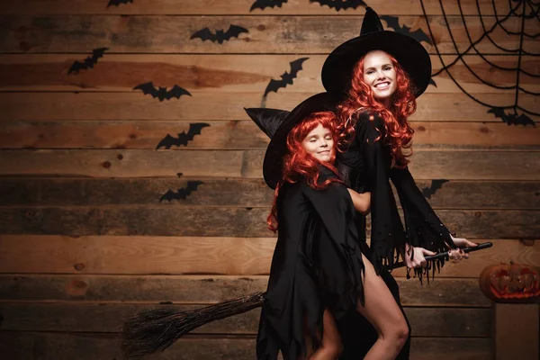 Halloween Concept - mooie Kaukasische moeder en haar dochter met lange rode haren in heks kostuums vliegen met magische bezemsteel. — Stockfoto