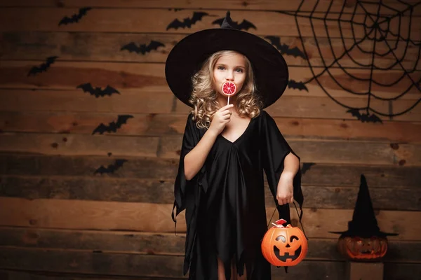 ハロウィーンの魔女の概念 - ハロウィーンの甘い小さな魔女子と元気な笑顔でお菓子。バットとクモの web 背景の上. — ストック写真