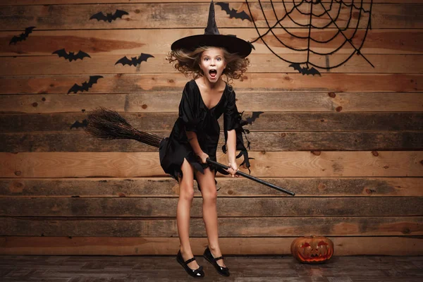 Απόκριες μάγισσα έννοια - παιδάκι Καυκάσιος μάγισσα που φέρουν σε μαγικό σκουπόξυλο πάνω από το ρόπαλο και spider web φόντο. — Φωτογραφία Αρχείου