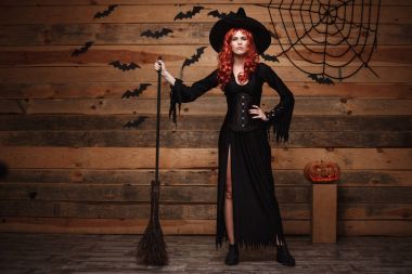 Halloween cadı kavramı - tam uzunlukta mutlu Cadılar Bayramı Kırmızı saçlı cadı holding sihirli süpürgesine eski ahşap studio arka plan üzerinde poz.