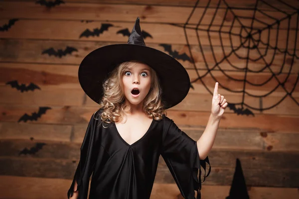 Halloween boszorkány koncepció - Vértes lövés kis kaukázusi boszorkány gyermek sokkoló arc jelentő denevér és a spider web studio fából készült háttér. — Stock Fotó