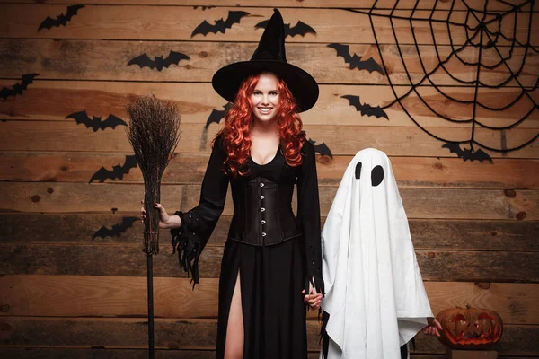 Koncepcja Halloween - matka czarownica i mały biały Duch robi Cukierek albo psikus z okazji Halloween pozowanie z zakrzywione dynie przez nietoperze i pajęczyna na podłoże drewniane studio. — Zdjęcie stockowe