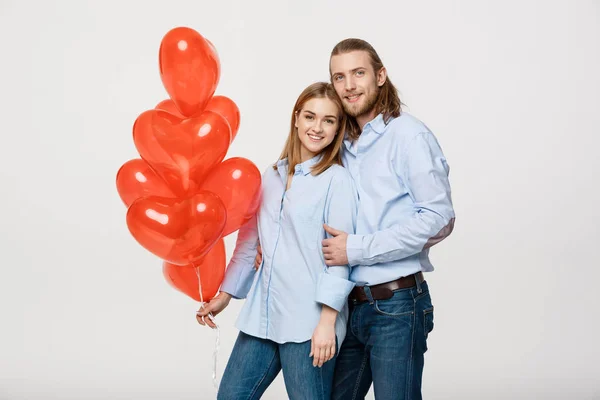Retrato de pareja caucásica joven de moda con globos corazón abrazándose unos a otros sobre un fondo blanco aislado . —  Fotos de Stock