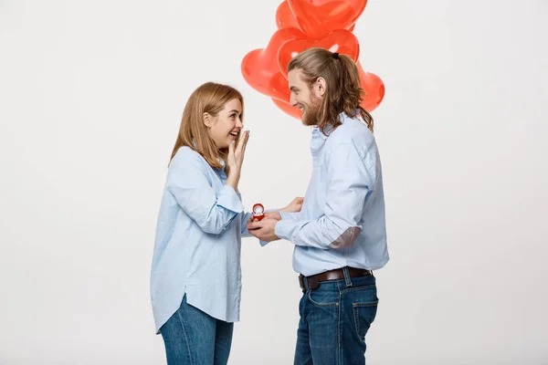 Retrato de joven chico guapo da un anillo a una chica sobre un fondo blanco con globos de aire rojo corazón . — Foto de Stock