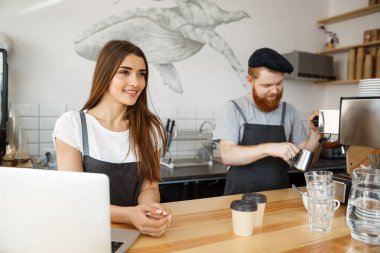 Kahve iş kavramı - pozitif genç sakallı dostum ve güzel çekici Bayan barista çift birlikte modern kahve dükkanında çalışmaktan hoşlanıyor