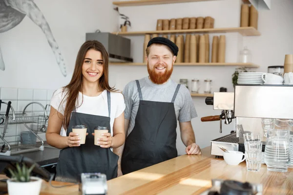 Coffee Business Concept - Positivo jovem barbudo homem e bela atraente senhora barista casal dando tirar xícara de café para custome no café moderno — Fotografia de Stock