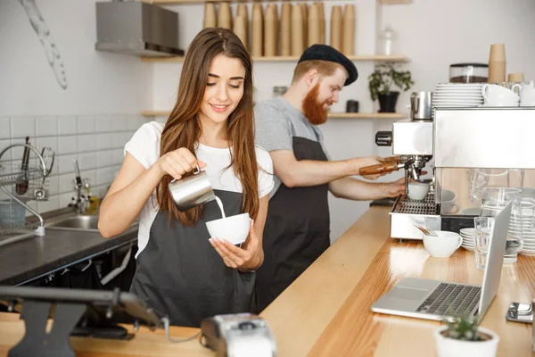 Conceito de negócio de café - close-up senhora barista no avental preparando e derramando leite em xícara quente enquanto está em pé no café . — Fotografia de Stock