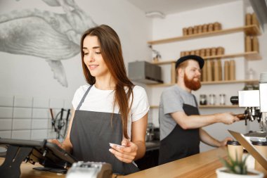 Kahve iş kavramı - müşterinin kredi kartı ile ödeme hizmet veren ve barda çalışırken gülümseyen güzel kadın barista modern kafede karşı.