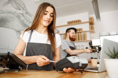 Kahve iş kavramı - müşterinin kredi kartı ile ödeme hizmet veren ve barda çalışırken gülümseyen güzel kadın barista modern kafede karşı.