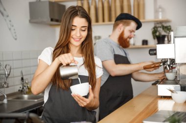 Kahve iş kavramı - yakın çekim Bayan barista önlük hazırlama ve kafede dururken sıcak fincan içine dökülen süt.