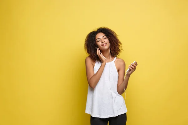 Lifestyle Concept - Πορτρέτο της όμορφης Αφροαμερικανής γυναίκας χαρούμενη ακούγοντας μουσική στο κινητό τηλέφωνο. Κίτρινο παστέλ φόντο στούντιο. Αντιγραφή χώρου. — Φωτογραφία Αρχείου
