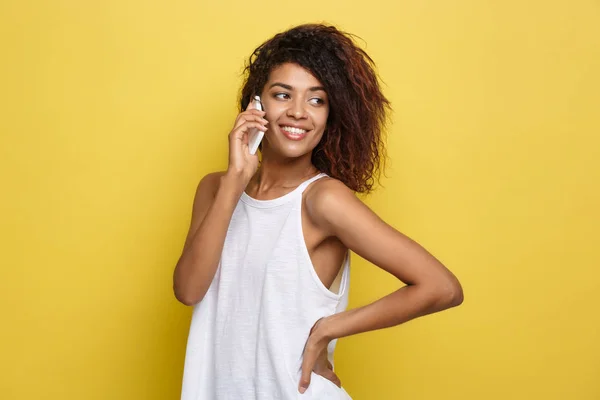 Concepto de estilo de vida - Retrato de una hermosa mujer afroamericana alegre hablando por teléfono móvil con un amigo. Fondo amarillo pastel estudio. Copiar espacio . — Foto de Stock
