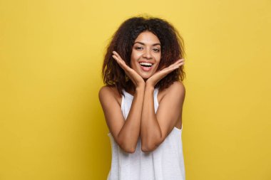Güzel genç eller beyaz T-shirt ile poz olarak Afrikalı-Amerikalı kadın çeneme gülümseyen. Stüdyo Sarı zemin üzerine vurdu. Kopya alanı.