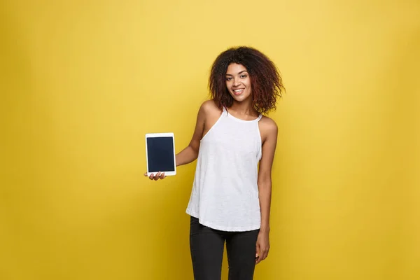 Lifestyle Concept - Retrato de la hermosa mujer afroamericana alegre presentando algo en la tableta electrónica. Fondo amarillo pastel estudio. Copiar espacio . — Foto de Stock