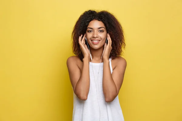 Lifestyle Concept - Portret van een mooie Afro-Amerikaanse vrouw die vrolijk luistert naar muziek op mobiele telefoon. Gele pastel studio achtergrond. Kopieer ruimte. — Stockfoto