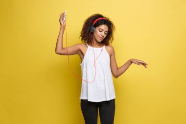 Yaşam Tarzı Konsepti - Cep telefonundan müzik dinleyen güzel Afro-Amerikan kadın portresi. Sarı pastel stüdyo arka planı. Boşluğu Kopyala