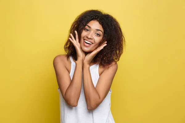 Glimlachend mooie jonge African American vrouw in het witte T-shirt poseren met op de kin handen. Studio opname op gele achtergrond. Kopiëren van ruimte. — Stockfoto